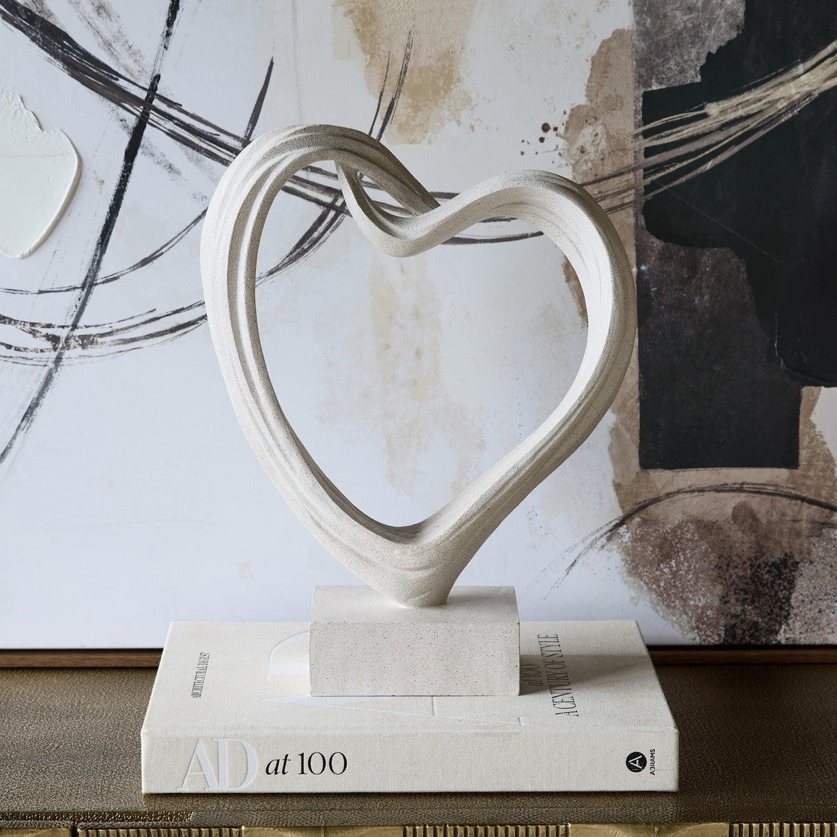 Libra Interiors Grainy Resin Abstract Heart Sculpture in white with a twisted open form on a square base, styled on an AD at 100 book by abstract artwork.