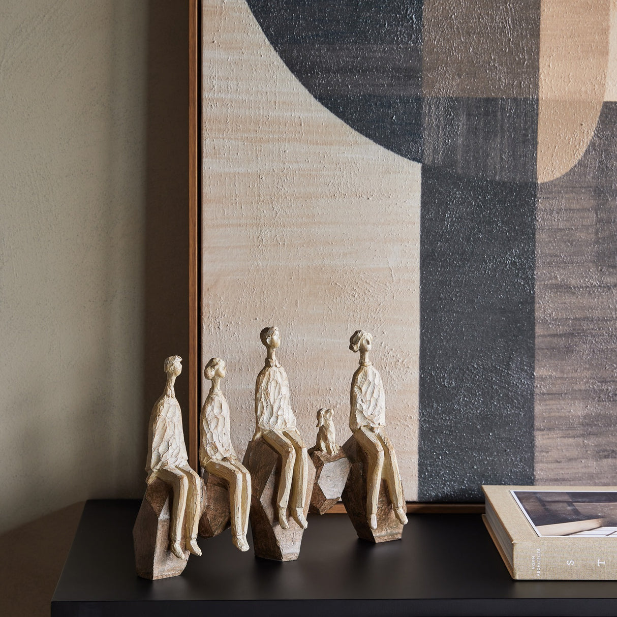 Libra Interiors Carved Resin Figural Family Sculpture in brown, five stylised figures and a dog on angular rocks, styled on a dark console with artwork.