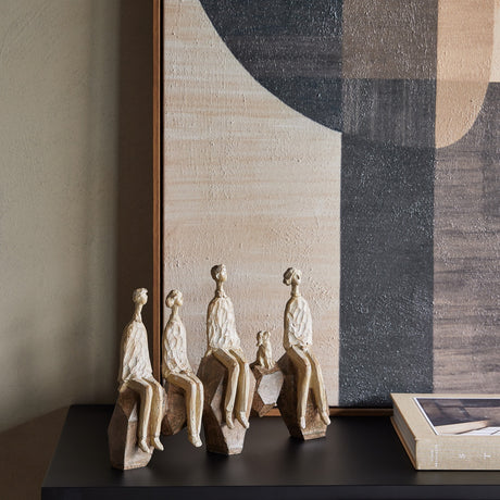 Libra Interiors Carved Resin Figural Family Sculpture in brown, five stylised figures and a dog on angular rocks, styled on a dark console with artwork.