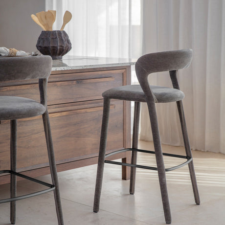 Libra Interiors Velvet Curved-Back Bar Stools in grey with low curved backrests and black powder coated footrests, set at a wooden kitchen island.