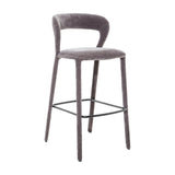 Libra Interiors Velvet Curved-Back Bar Stool in grey with padded seat, low curved backrest, upholstered legs and black powder-coated steel footrest.