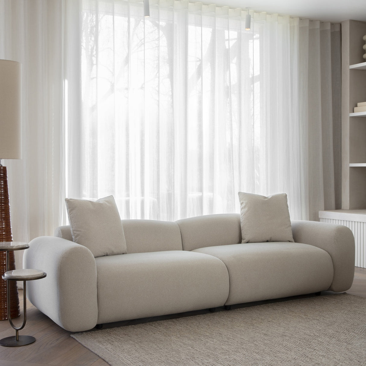 Libra Interiors Brushed Velvet 3 Seater Modular Sofa in cream with rounded arms and two matching cushions, styled in a living room by sheer curtains.