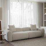 Libra Interiors Brushed Velvet 3 Seater Modular Sofa in cream with rounded arms and two matching cushions, styled in a living room by sheer curtains.