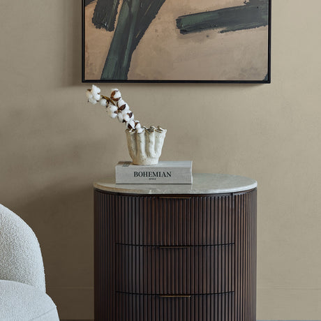 Libra Interiors Fluted Walnut Marble-Top Bedside Table in brown styled with a cotton stem in a ceramic vase and Bohemian Style book beneath abstract art.