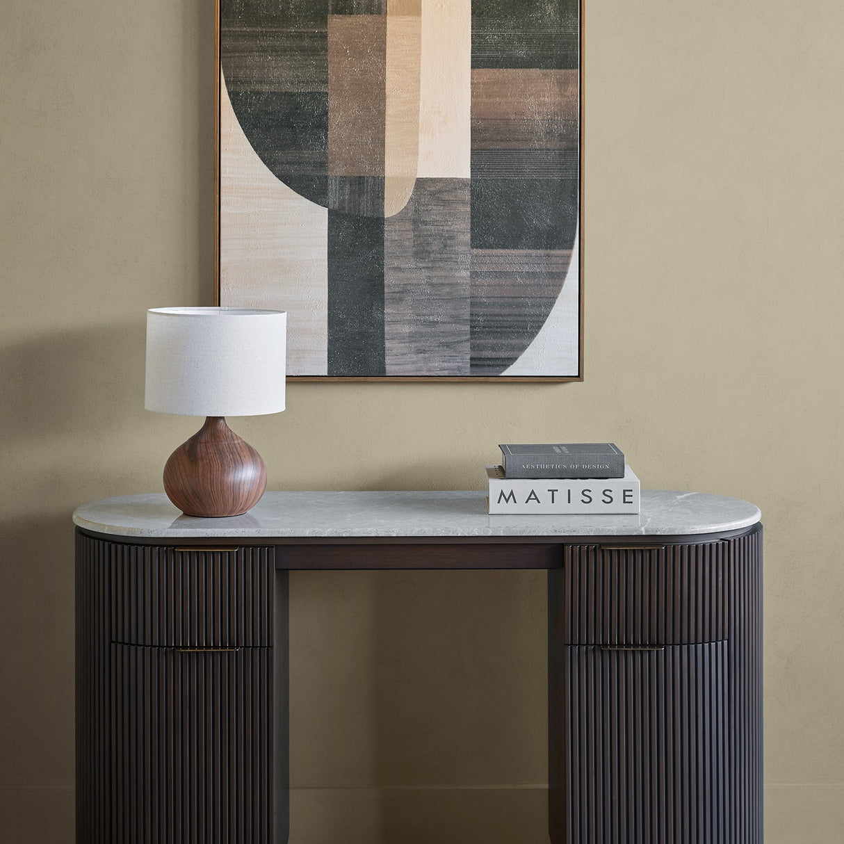 Libra Interiors Marble Top Fluted Walnut Pedestal Desk in brown styled with a wooden lamp and Matisse books beneath a geometric artwork.