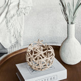 Libra Interiors Openwork Starfish Aluminium Decorative Bowl in beige, styled on a book atop a wooden tray beside a textured white vase with foliage.