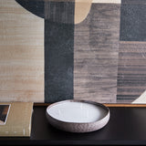 Libra Interiors hammered aluminium three-wick bowl candle in brown with white wax, on a dark console beside a book and abstract artwork.