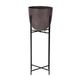 Libra Interiors Hammered Aluminium Raised Planter in brown, a curved matt stonewash pot set on a tall slim black iron four-leg stand, on a white background.
