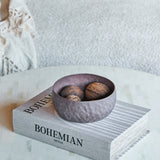 Libra Interiors Hammered Stonewash decorative aluminium bowl in brown, holding dried seed pods, set on a Bohemian Style book atop a pale inlaid coffee table.