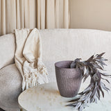 Libra Interiors hammered stonewash aluminium tapered planter in brown on a light mosaic coffee table, holding dark foliage beside a bouclé sofa and throw.