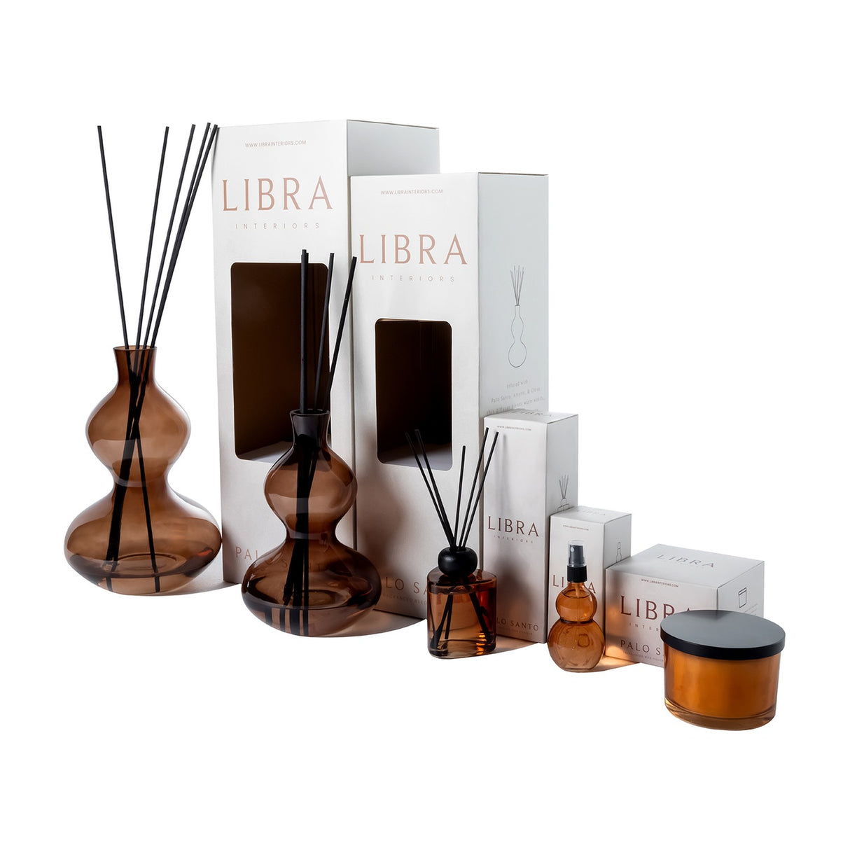 Libra Interiors Sculptural Glass Reed Diffuser in brown, shown in two sizes with black reeds beside white Palo Santo packaging, spray and candle on white.