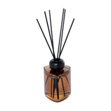 Libra Interiors Amber Glass 200ml Reed Diffuser in brown with a triangular amber bottle, rounded black collar and slim black fibre reeds, on white.