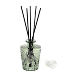 Libra Interiors Embossed Glass Reed Diffuser in soft green tinted glass with black reeds and a spherical glass stopper set beside it on a white background.