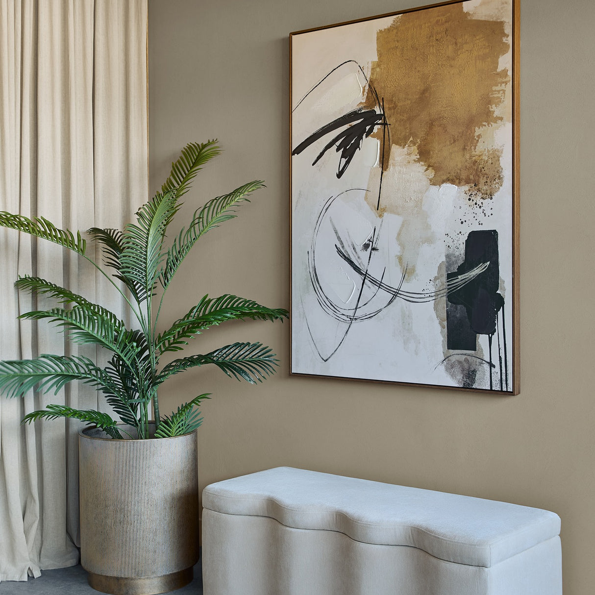 Libra Interiors Velvet Lift-Top Storage Ottoman in cream with a softly curved top, set in a hallway beside a potted palm and abstract wall art.