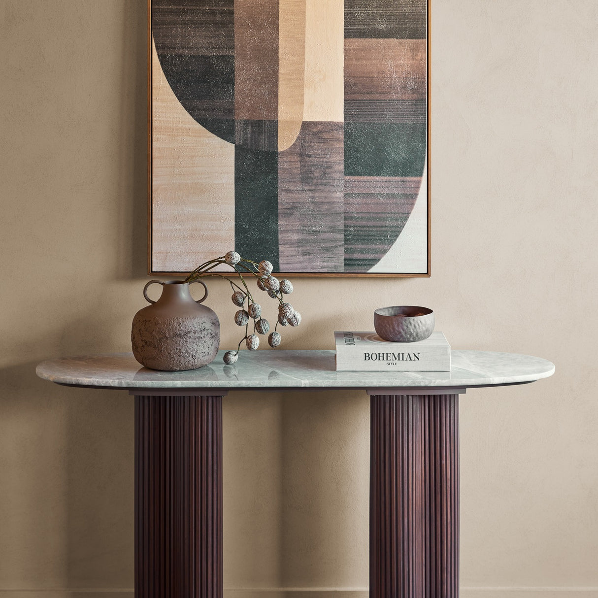 Libra Interiors Marble Top Fluted Walnut Console Table in brown with oval grey marble top, styled with a vase, book and bowl below abstract art.