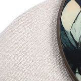 Close-up of Libra Interiors Printed Glass Nesting Coffee Table with oatmeal cobble-textured fabric pouffe beside bronze-framed printed leaf glass top.