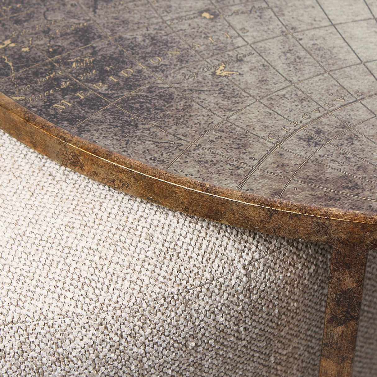 Close-up of Libra Interiors Round Map-Print Glass Nesting Coffee Table with printed world map top, brass-toned iron frame and woven fabric pouffe beneath.