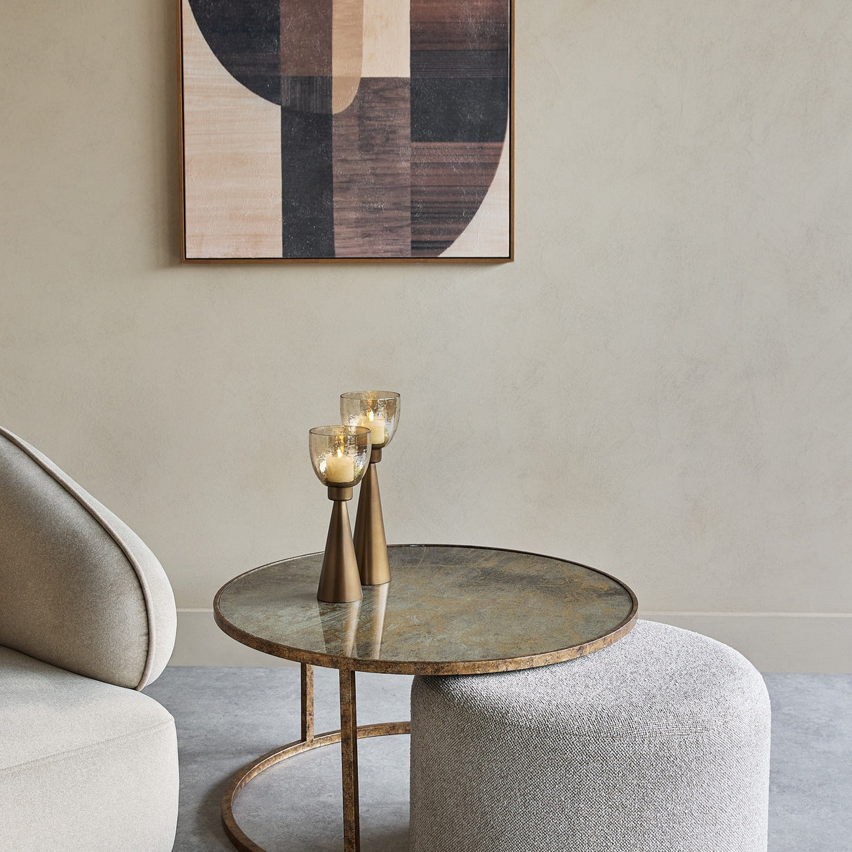 Libra Interiors Round Map-Print Glass Nesting Coffee Table with brass-toned frame and grey cobble-weave pouffe, styled with candle holders in a living room.