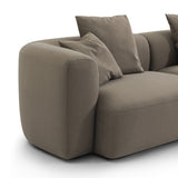 Close-up of the Libra Interiors Velvet Curved 2-Seater Modular Sofa in truffle, showing the rounded arm, deep seat and loose scatter cushions.