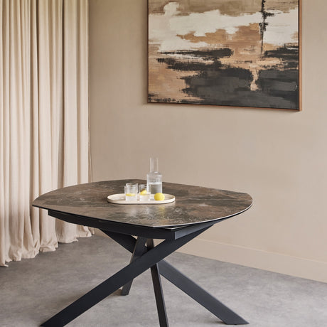 Libra Interiors extendable dining table with smoked grey ceramic stone-effect top and matt black intersecting metal legs, styled in a neutral dining room.