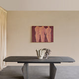 Libra Interiors Extendable Ceramic Stone Effect Dining Table in black with bronze veining and dark pedestal legs, styled with a vase beneath figurative artwork.