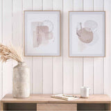 Set of 2 natural abstract canvas wall art prints in thin wood frames, shown above a wooden console table with a textured vase and white mug.