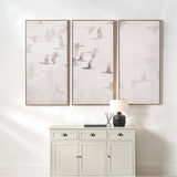 Set of 3 framed canvas wall art panels with flying bird motifs in natural and white tones, hung above a white cabinet in a neutral-toned room.