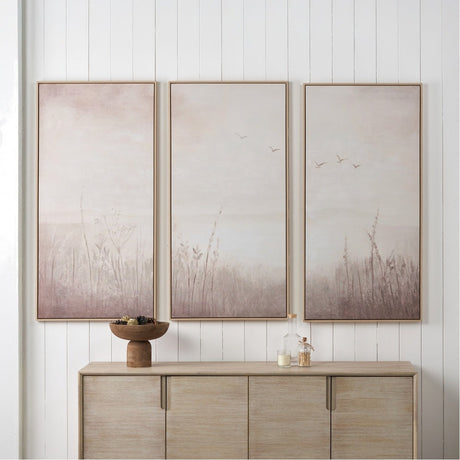 Set of 3 wood-framed canvas wall art panels in natural and white tones, depicting misty grasses and birds, displayed above a wooden sideboard.