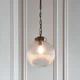 Endon Ashmere pendant light with ribbed clear glass globe shade and antique brass chain suspension, hung against a white panelled wall.