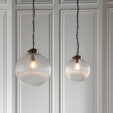 Endon Ashmere pendant lights in two sizes with ribbed clear glass globe shades and antique brass chains, hung against a white panelled wall.