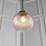 Endon Ashmere pendant light with ribbed round clear glass globe shade and antique brass chain suspension against white panelled wall.