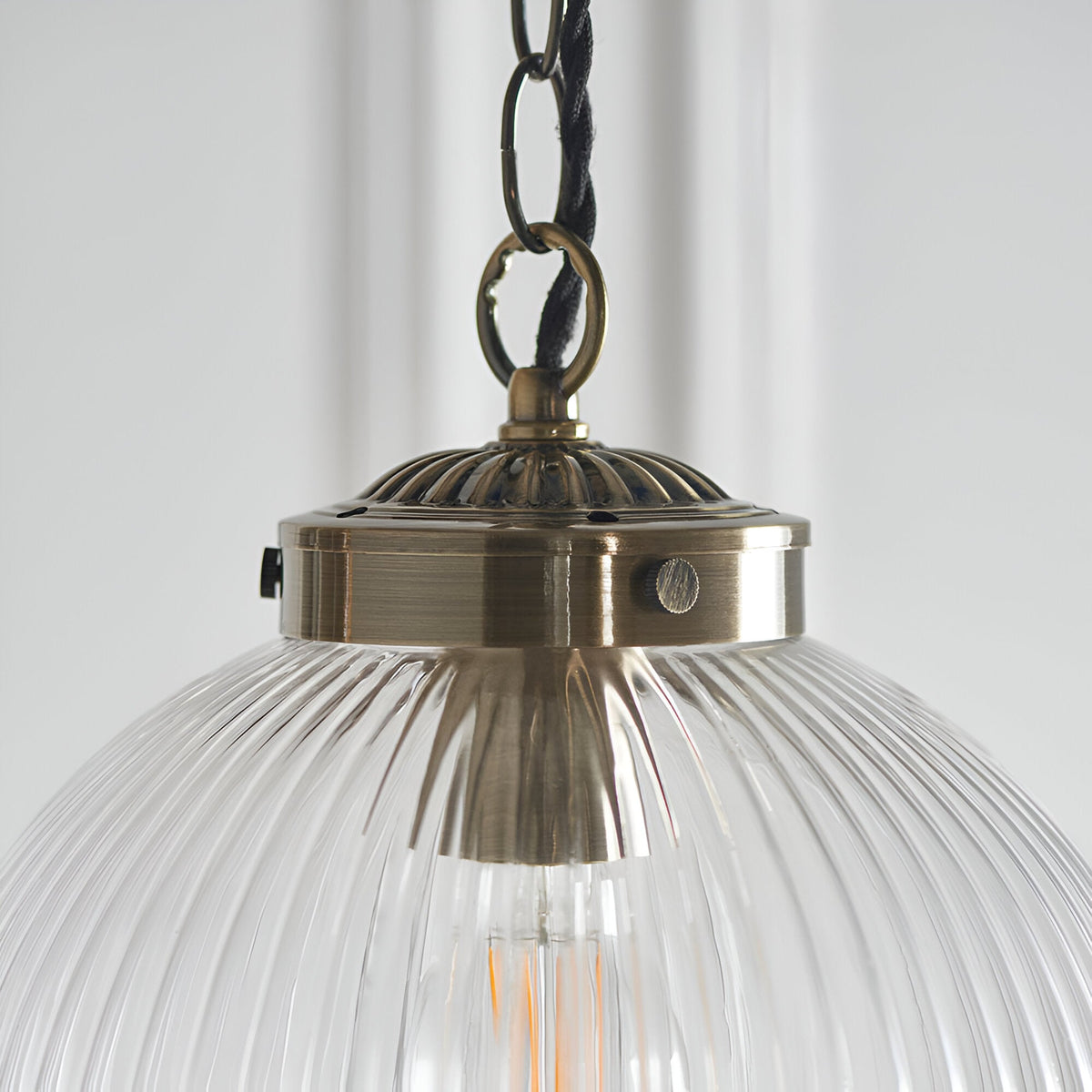 Close-up of the Endon Ashmere pendant showing the antique brass fitting, decorative cap and chain link above a ribbed clear glass shade.