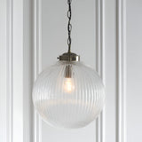 Endon Ashmere Large pendant light with ribbed round clear glass globe shade and antique brass chain suspension, mounted against a white panelled wall.