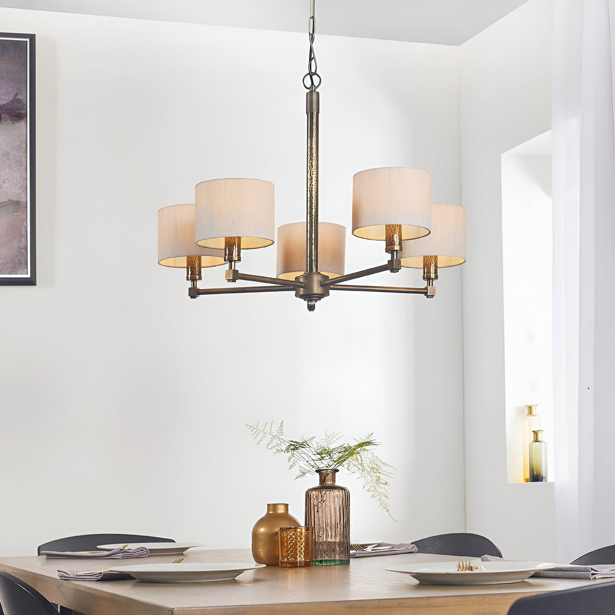 Endon Brenwood 5 light pendant in bronze with hammered central column and natural linen drum shades, hanging above a dining table in a bright room.