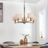 Endon Brenwood 5 light pendant in bronze with hammered central column and natural linen drum shades, hanging above a dining table in a bright room.