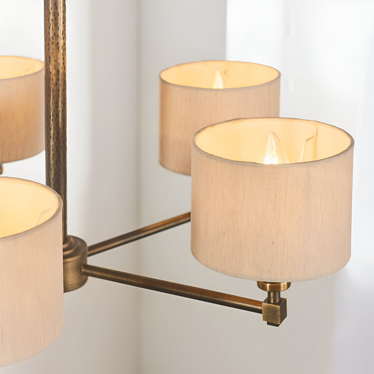 Close-up of Endon Brenwood 5 Light Pendant showing natural linen effect drum shades and hammered bronze arms with lit E14 bulbs against a white wall.