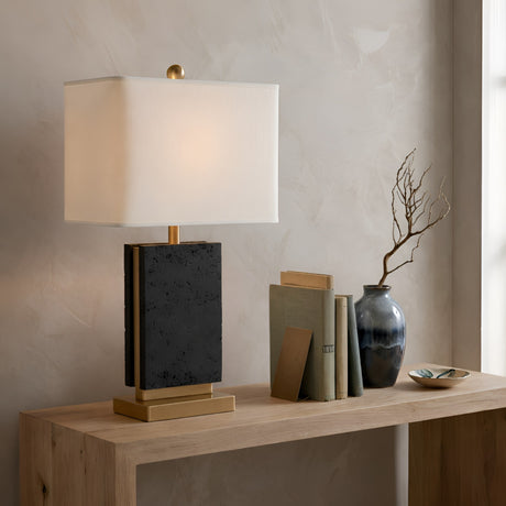The Forma 1 Light Marble Table Lamp in white and black features a rectangular white shade and sits on a light wooden console beside stacked books, a dark vase with a bare branch, and a small decorative bowl against a textured beige wall.