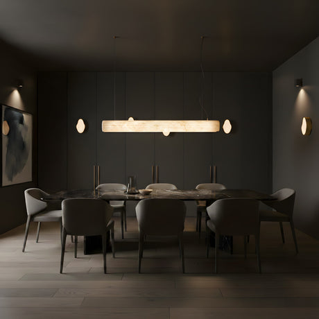 A modern dining room with dark walls and a rectangular marble table, eight gray chairs, and the Zenvia LED Alabaster Suspension Light – Soft White overhead, plus subtle wall sconces for a minimalist, moody ambiance.