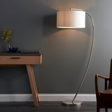 Brockfield Floor Lamp in polished nickel with an arched metal stem and oversized white drum shade, shown lit beside a wooden console table.