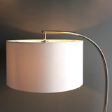 Brockfield Floor Lamp in nickel, close-up of the curved polished nickel arm and large drum-shaped white faux silk shade, against a grey background.