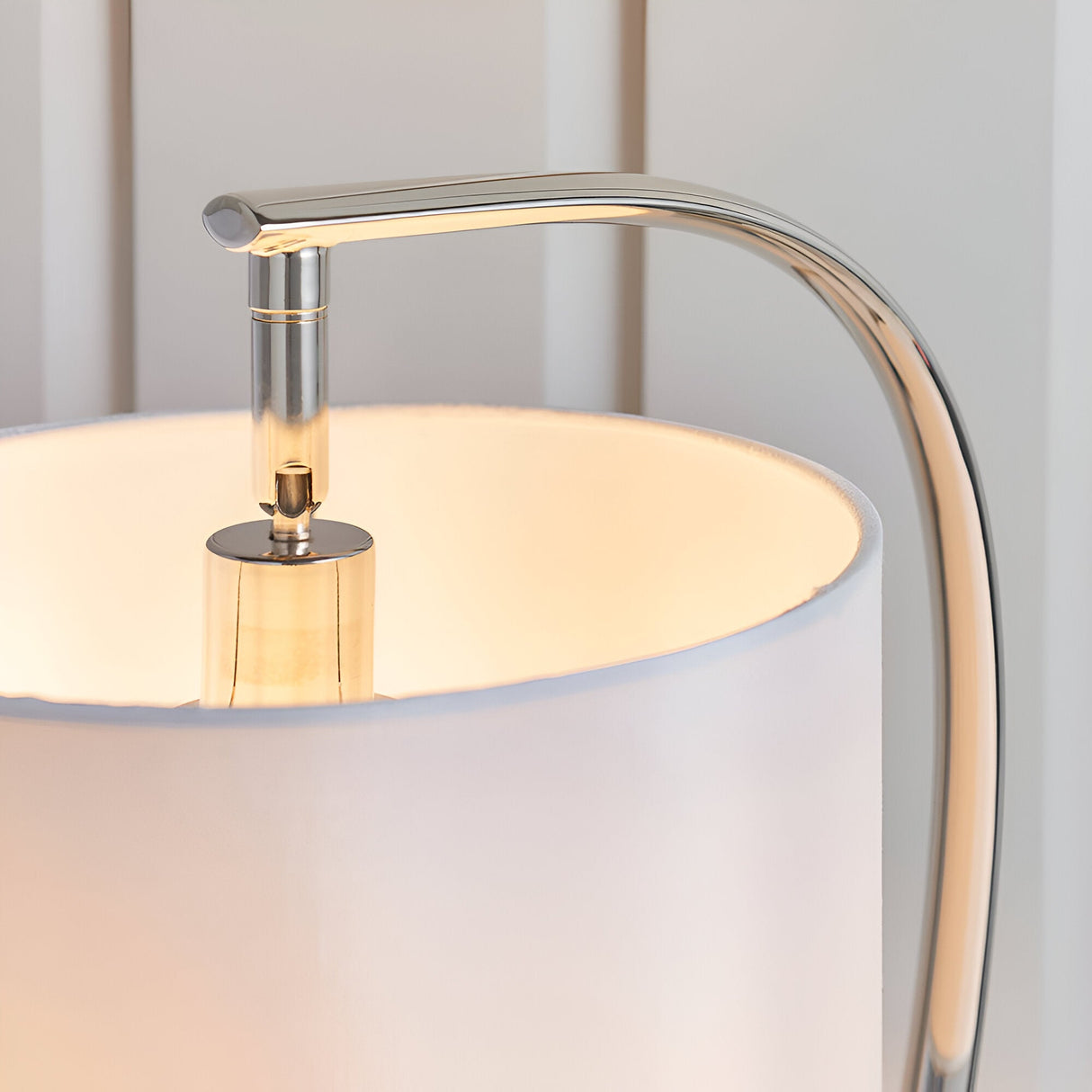 Close-up of the Brockfield Table Lamp in nickel, showing the curved metal arm and E14 bulb fitting above a white faux silk shade.
