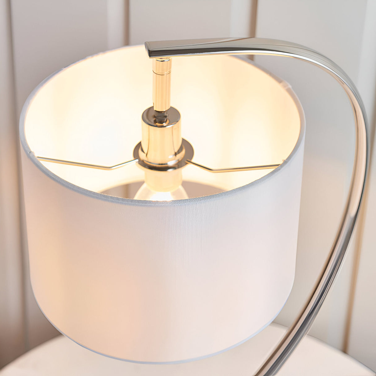 Close-up of the Brockfield Table Lamp's white faux silk shade with curved nickel stem and E14 bulb visible inside, lit against a light background.