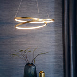 Endon Cliffley gold leaf ring pendant with integrated LED loop, suspended above a ribbed blue glass vase against a textured dark blue wall.