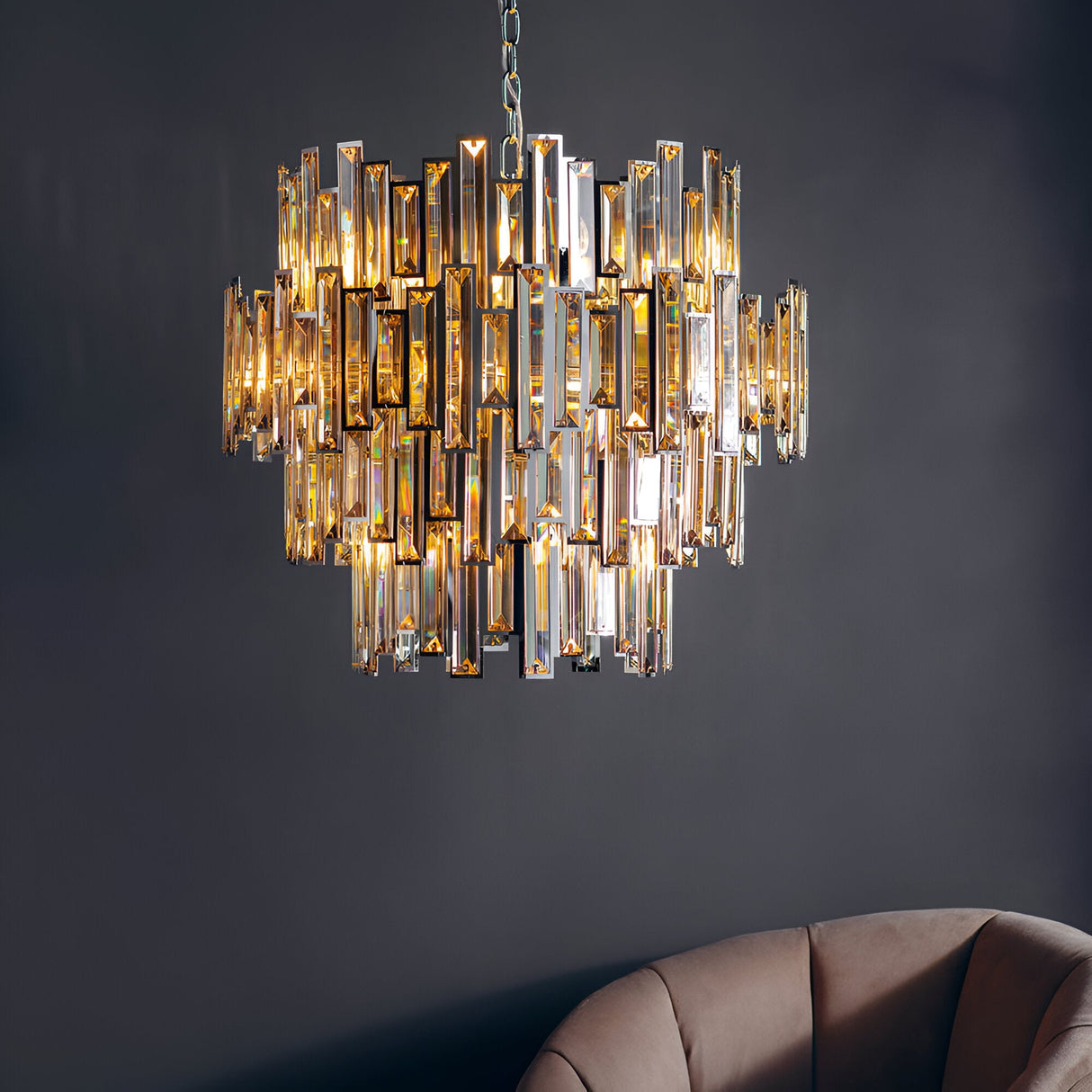 Endon Danedale 15 light polished chrome chandelier with tiered champagne bevelled crystals, lit above a beige armchair against a dark grey wall.