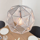 Aldford Pendant in polished chrome, a geometric mesh-triangle shade with visible bulb, hanging above a dining table in a light-toned room.