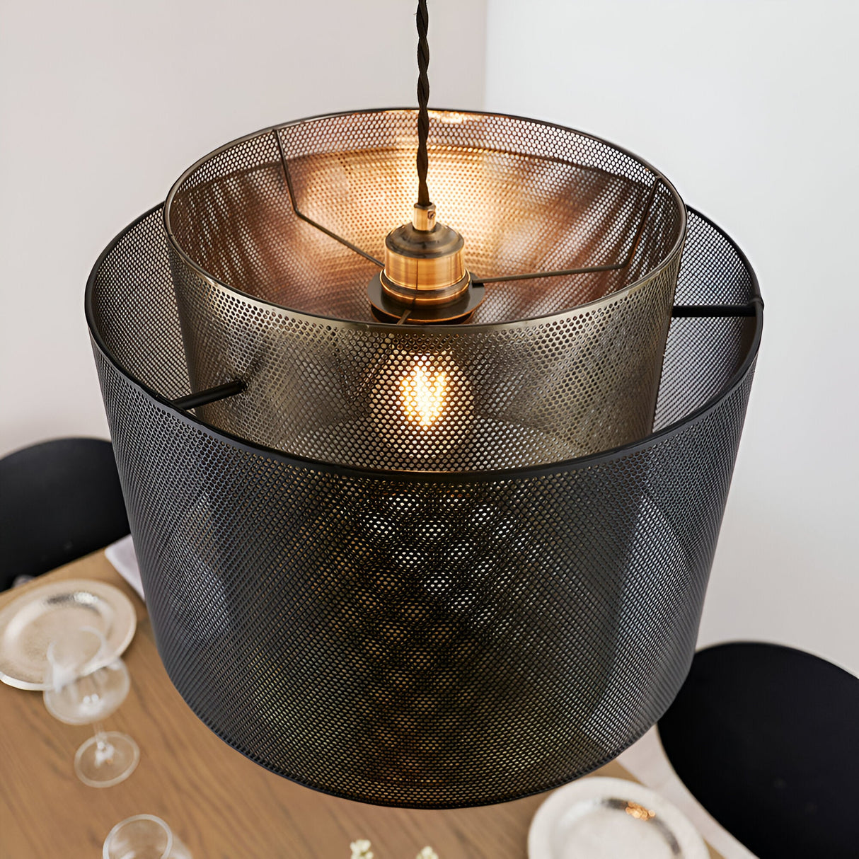 Chartfield Pendant in Brass & Black, showing nested mesh metal cylinder shades with antique brass inner and matt black outer layer, lit above a dining table.