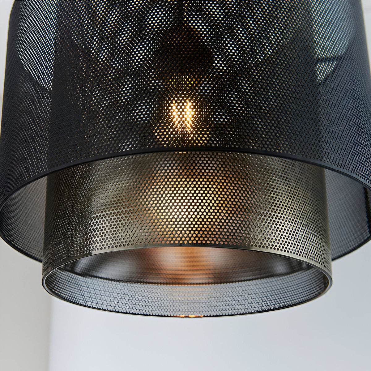Close-up of the Chartfield Pendant's mesh cylinder shade in matt black and antique brass, showing a glowing E27 bulb through the perforated metal.