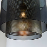 Close-up of the Chartfield Pendant's mesh cylinder shade in matt black and antique brass, showing a glowing E27 bulb through the perforated metal.