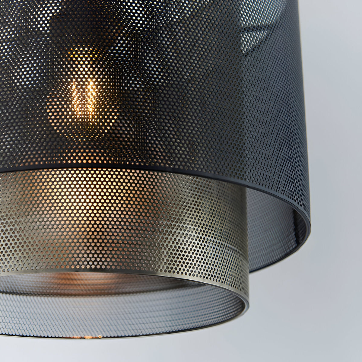 Chartfield Pendant close-up showing perforated black outer shade and antique brass inner cylinder with visible E27 bulb, set against a plain light background.