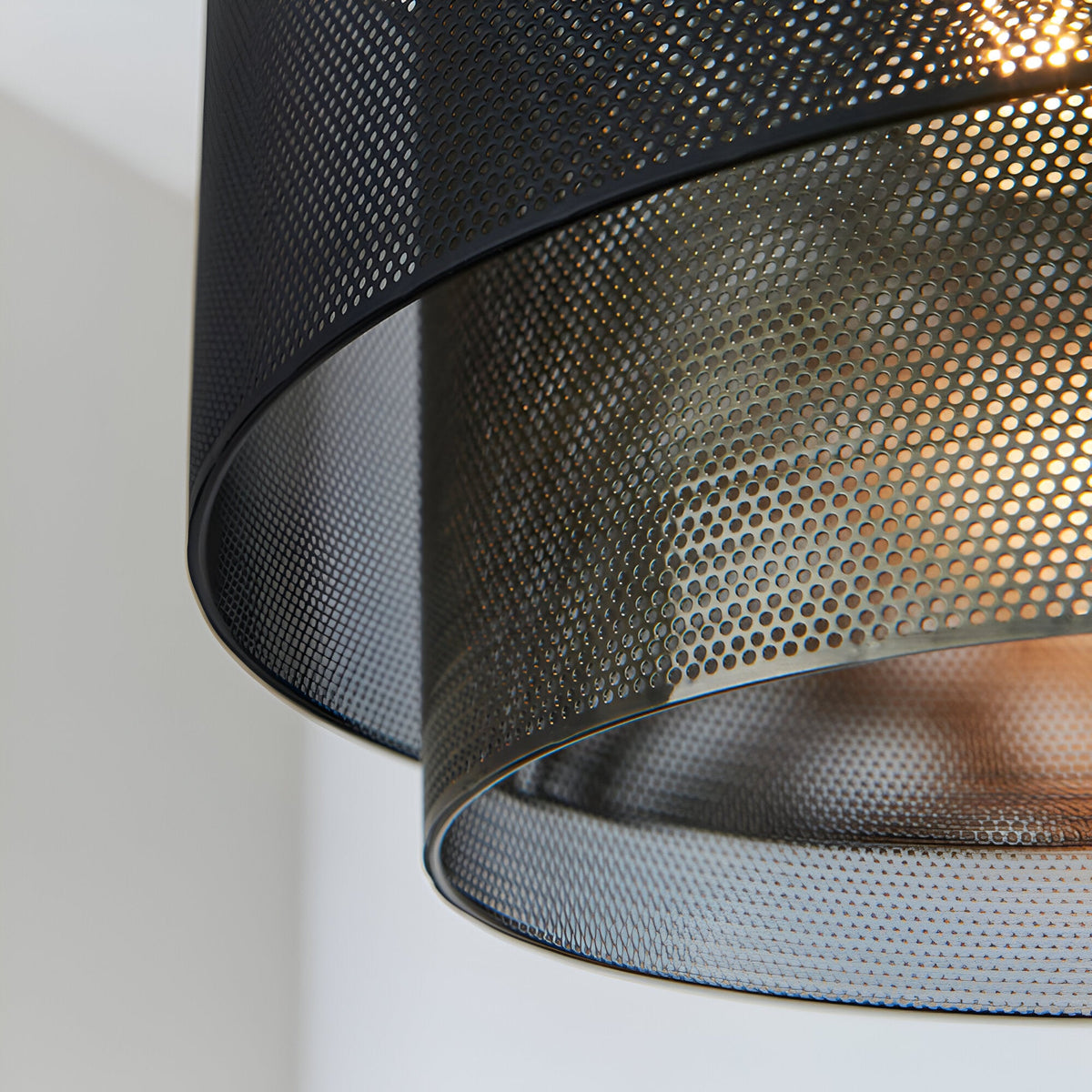 Close-up of the Chartfield Pendant in matt black perforated metal with an inner antique brass mesh shade, glowing E27 bulb visible through the pattern.